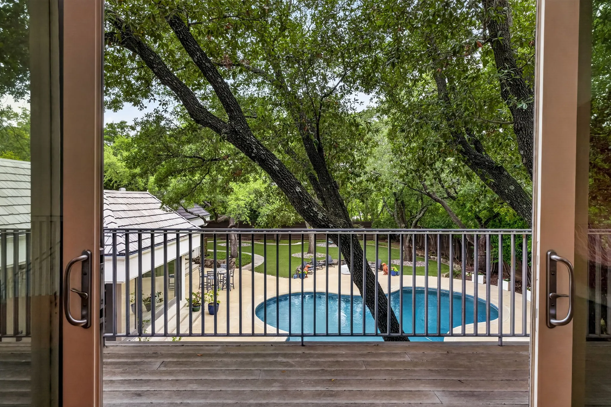 Patio doors opening to an outdoor living space featuring a wood-finish deck, metal railing, and a freeform swimming pool