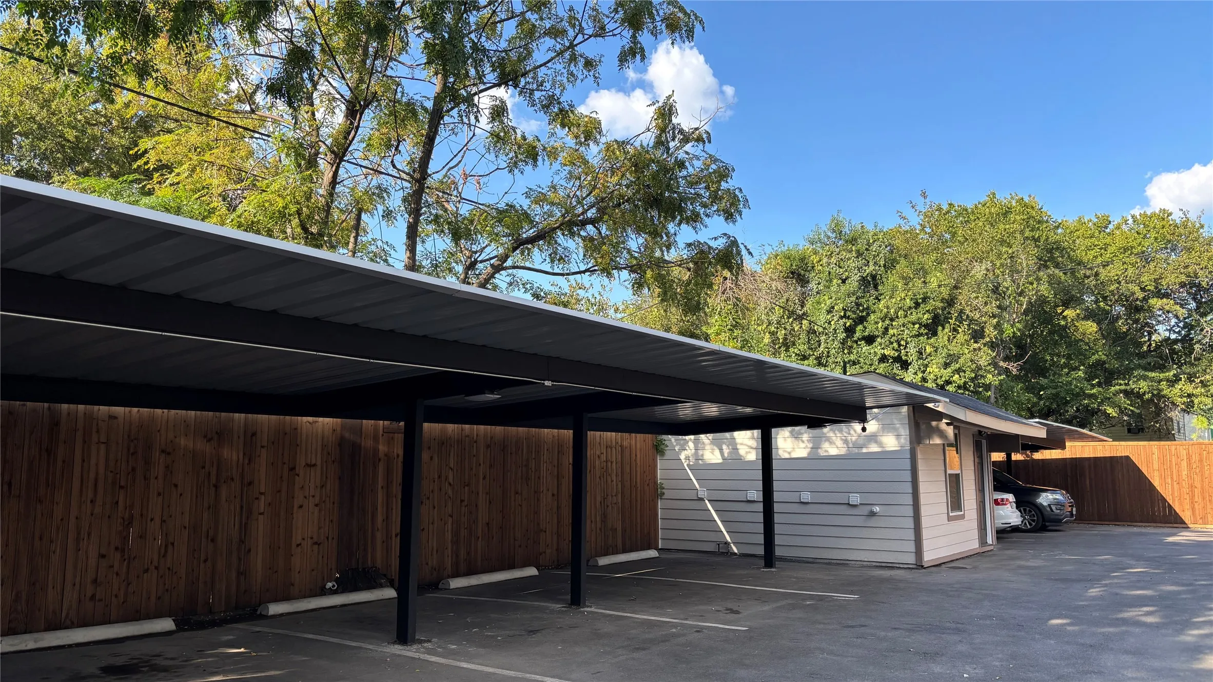 Expansive paved parking area with covered carport spaces featuring a corrugated metal roof and black support beams
