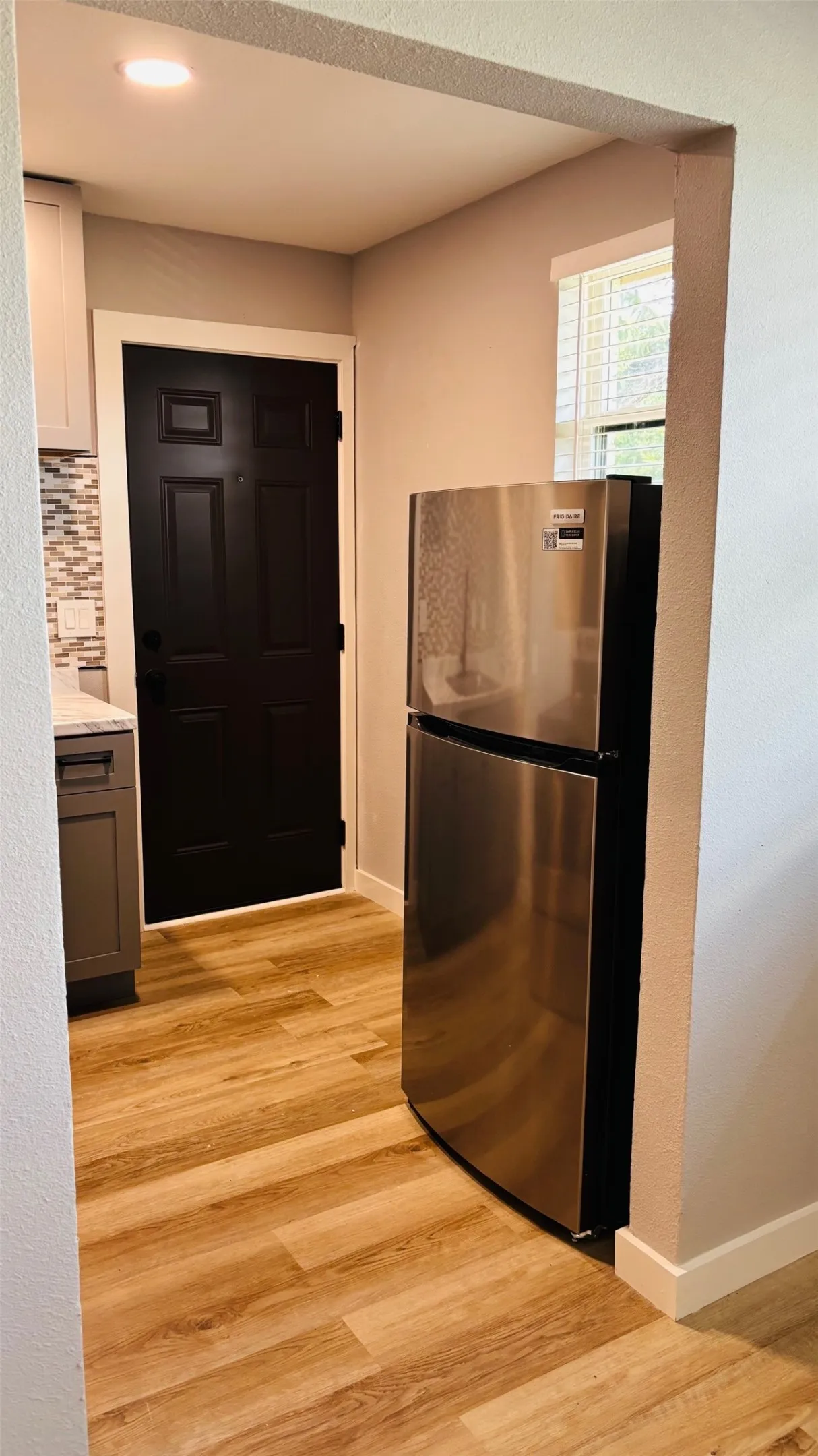 Kitchen area featuring wood-finish flooring, a stainless steel refrigerator, and a mosaic tile backsplash