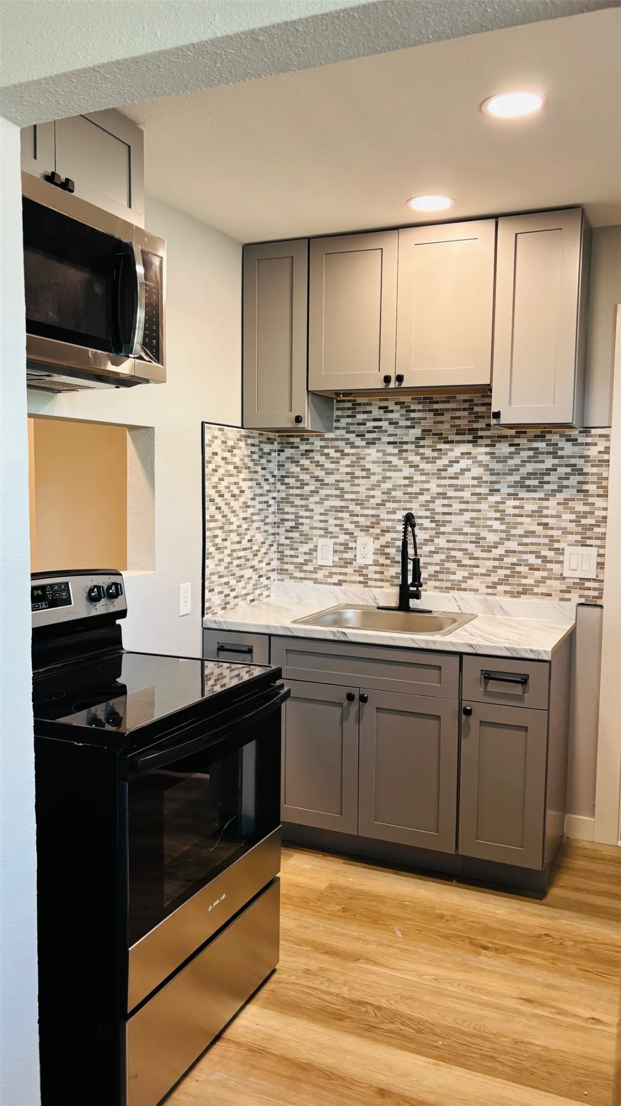 Contemporary kitchen featuring light gray cabinetry, mosaic tile backsplash, stainless steel appliances, and wood-finish flooring
