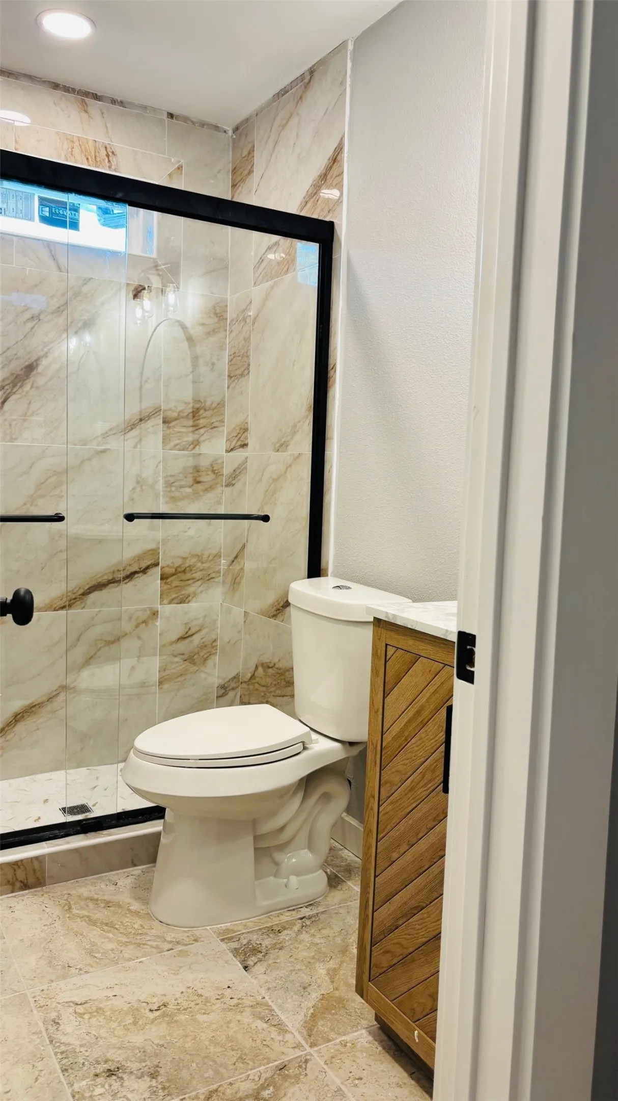 Bathroom featuring a walk-in shower with a black-framed glass enclosure, marble-patterned tile, and a recessed window