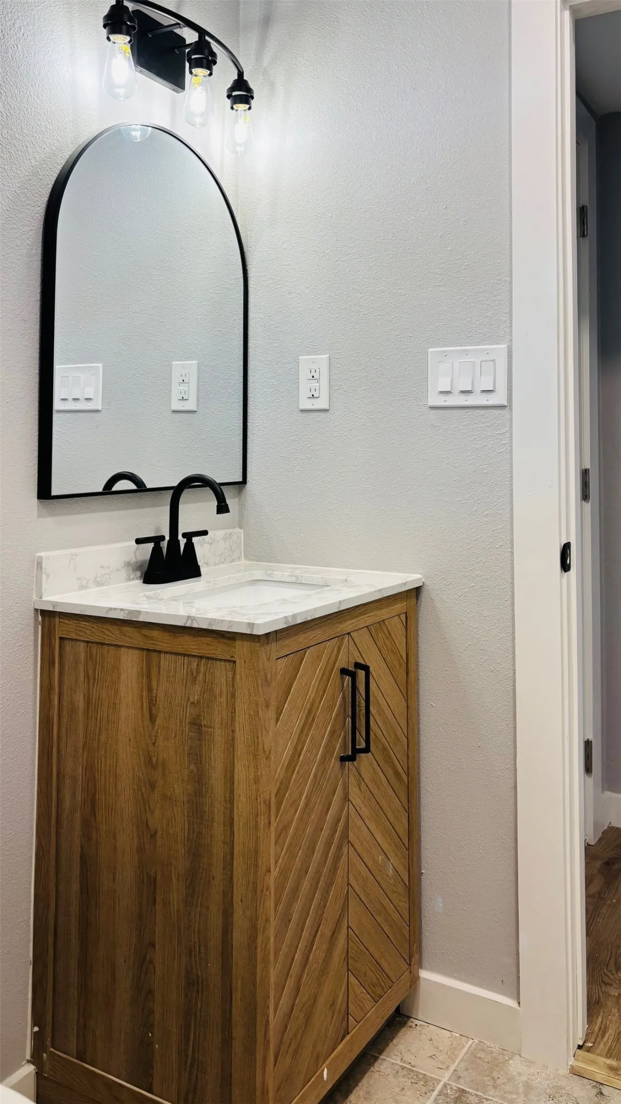 Bathroom vanity featuring a wood-finish cabinet with chevron paneling, a white countertop, and a black faucet