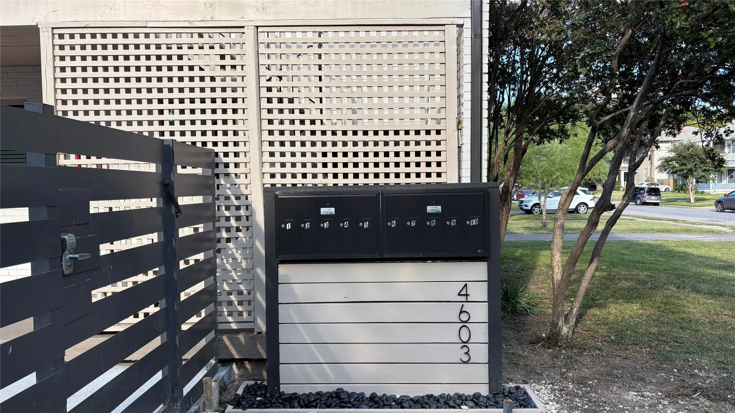 Modern community mailbox station featuring black individual mailboxes and light-toned horizontal siding with prominent numbering