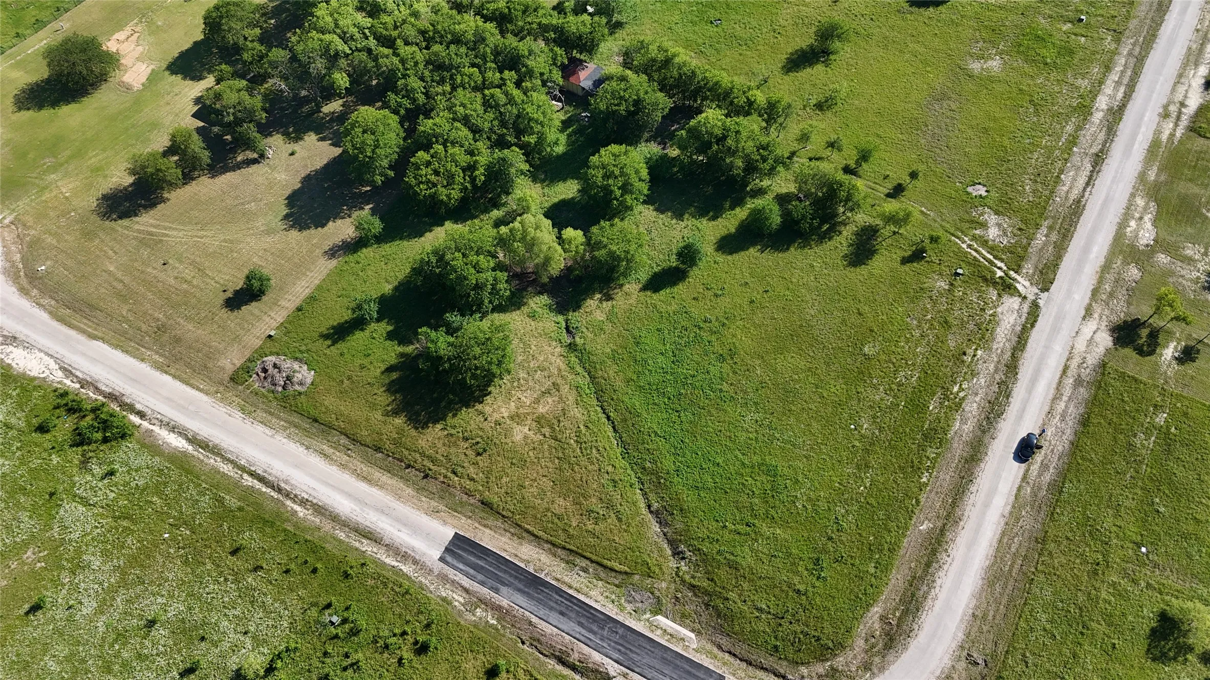 Expansive corner lot featuring a combination of asphalt and gravel road frontage, mature trees, and open green spaces