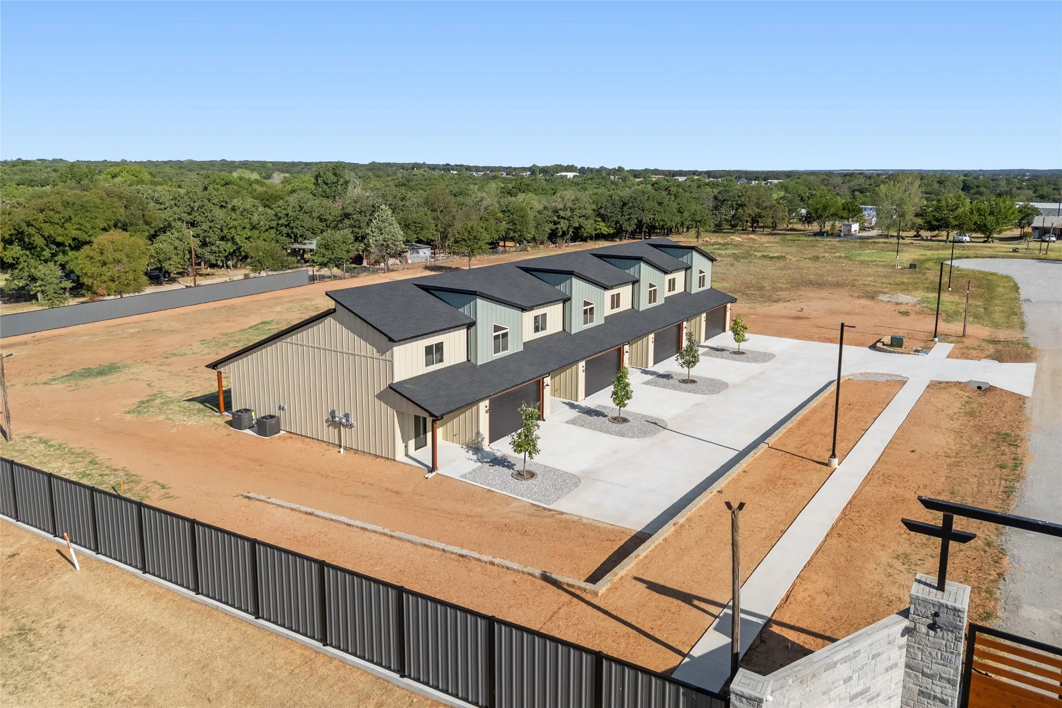 Multi-unit residential structure with individual garage doors, paved parking areas, and a stone-clad entry column