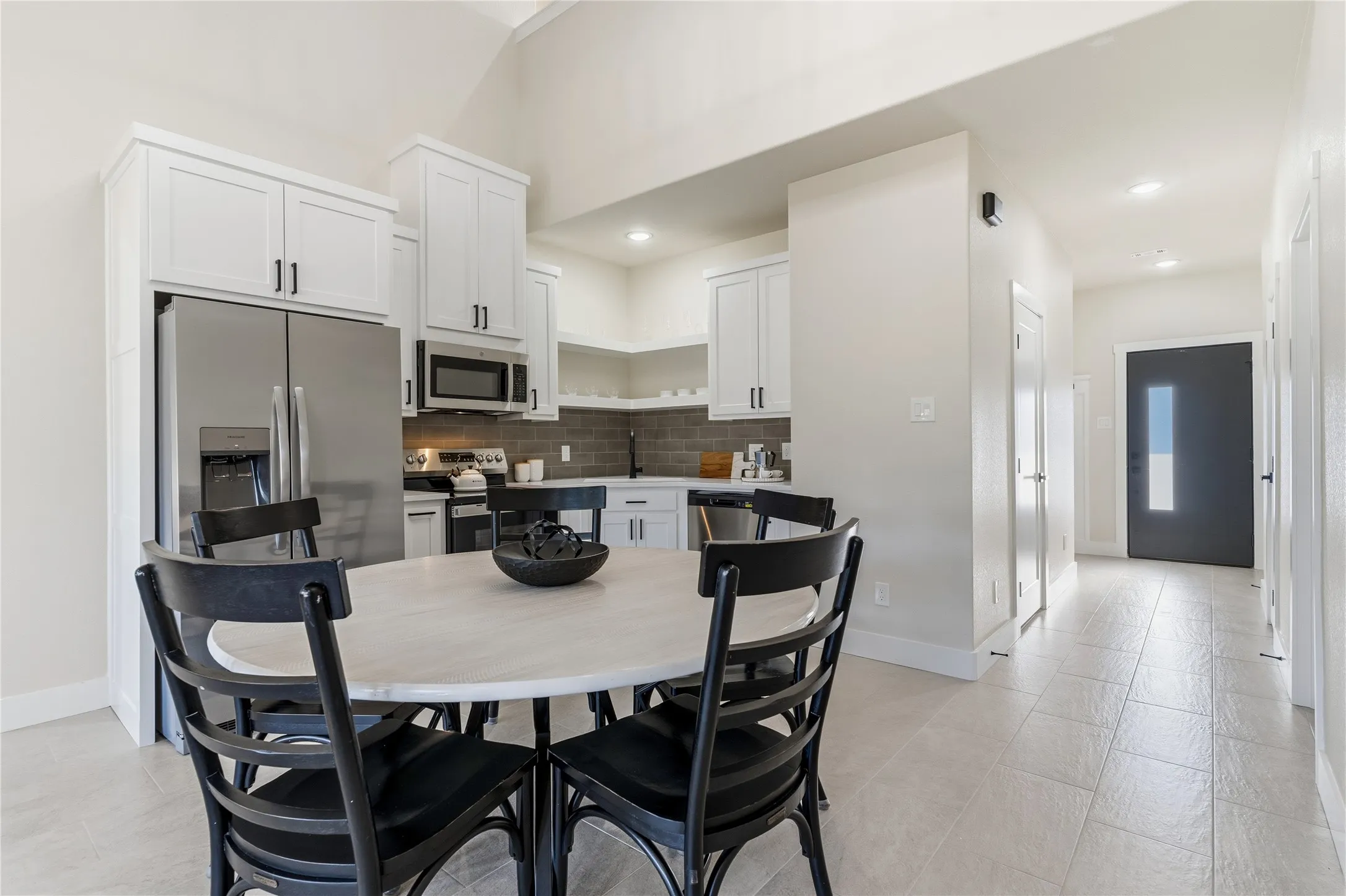 Kitchen with stainless steel appliances, white cabinetry, and dark subway tile backsplash