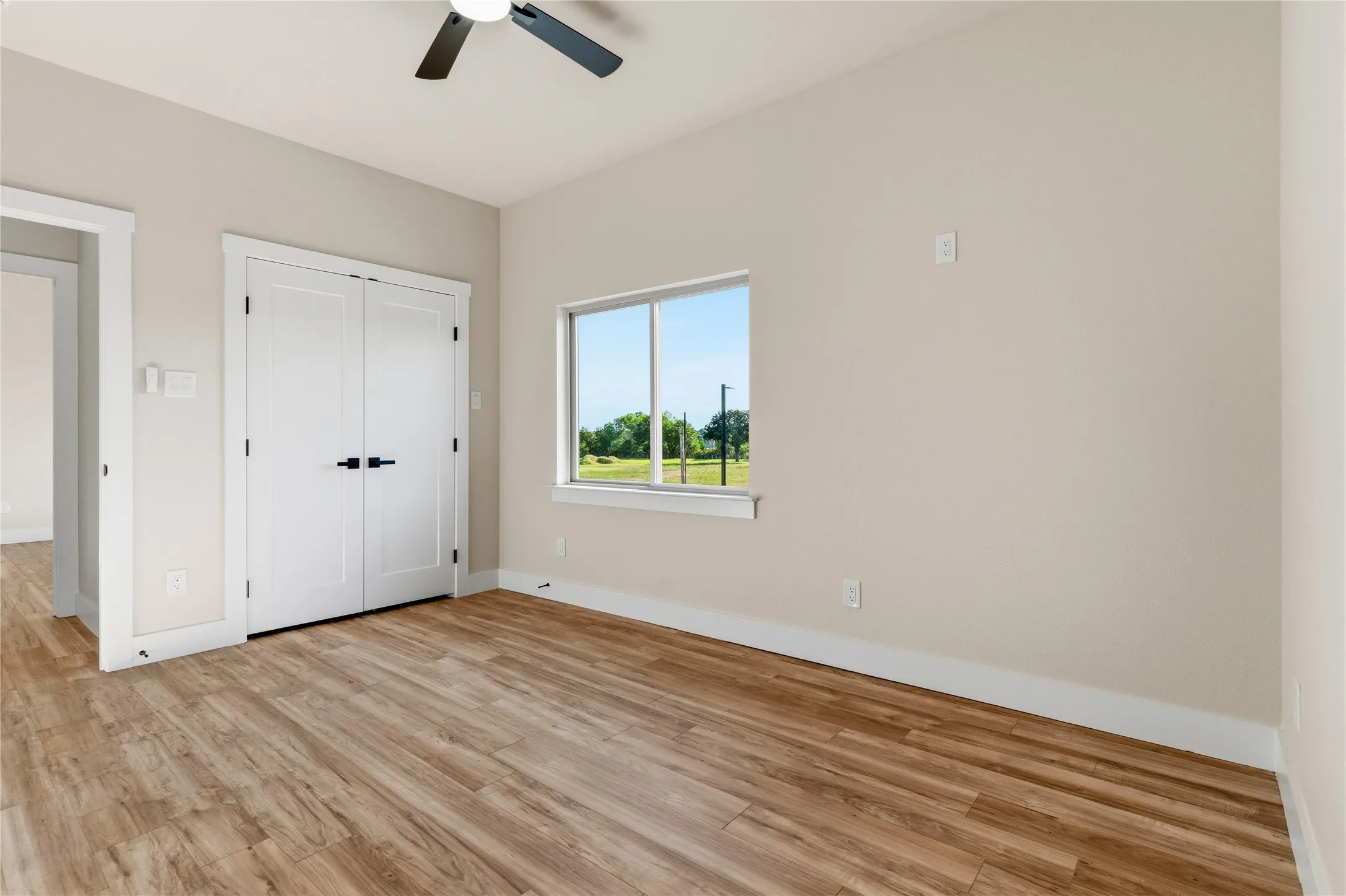 Wood-finish flooring, white trim, ceiling fan, and white double doors