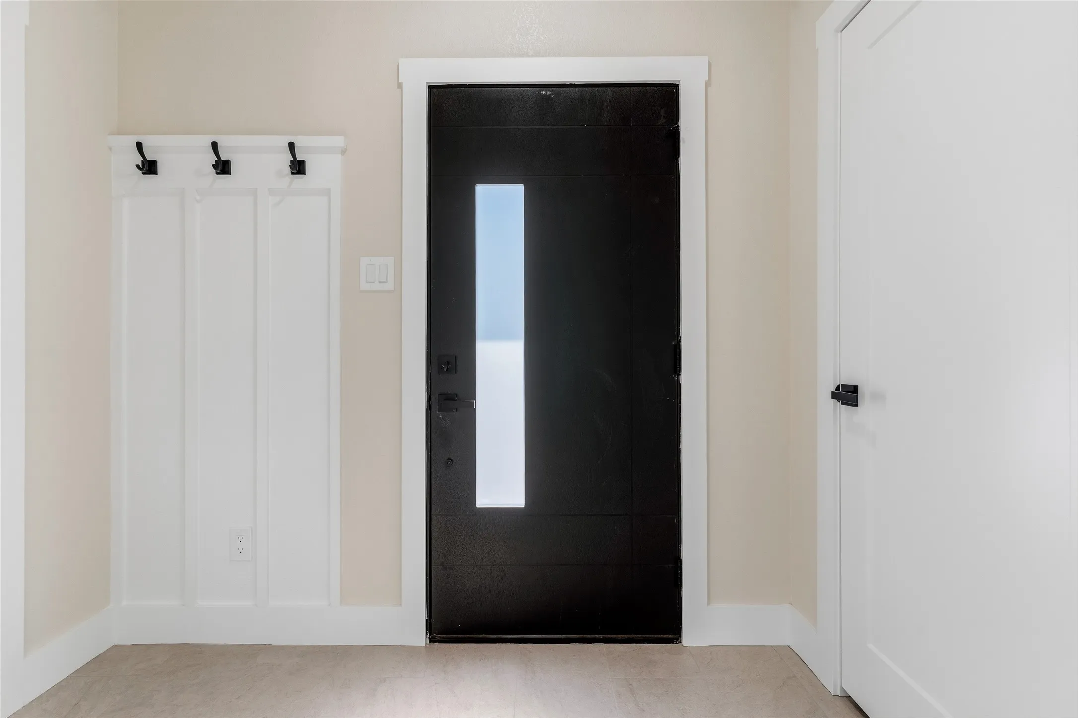 Black entry door with frosted glass insert, white interior door, and built-in coat rack with matte black hooks