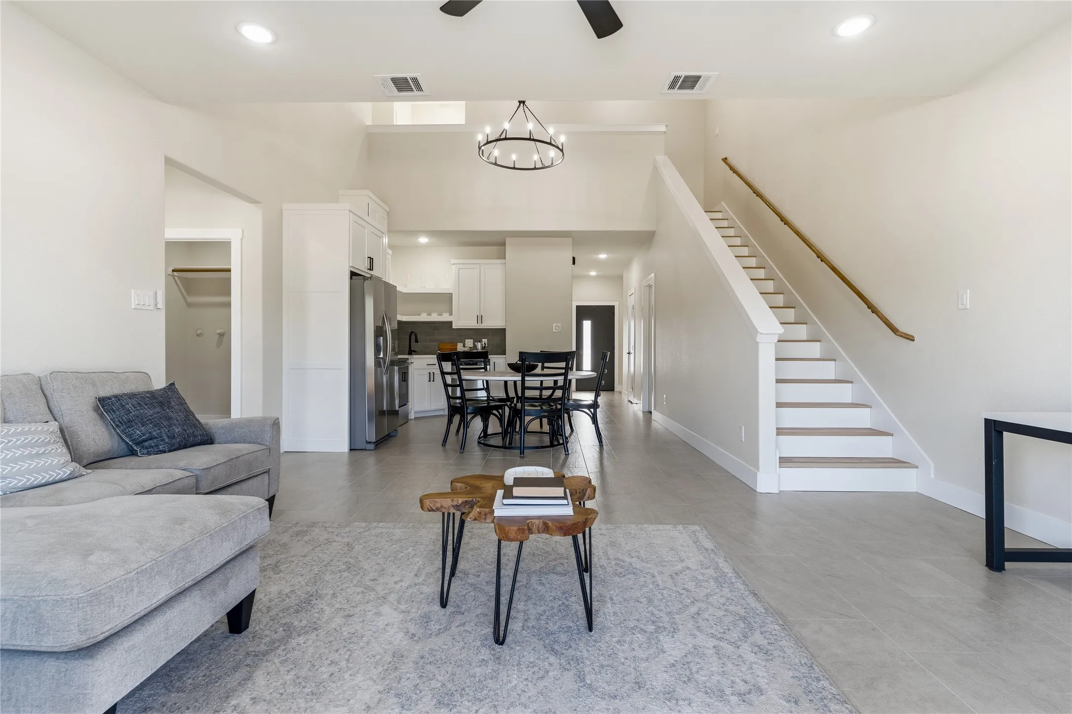 Open-concept living space featuring high ceilings, light-toned flooring, a staircase with a wooden handrail, and recessed lighting