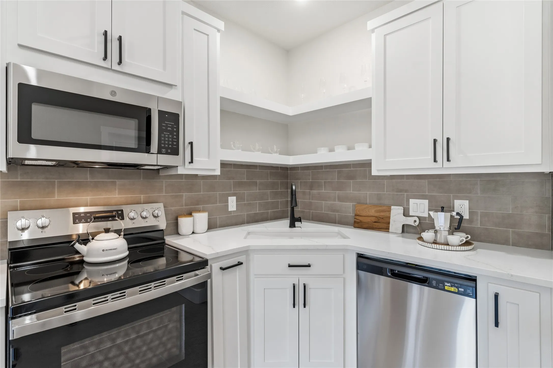 White shaker-style cabinetry, stainless steel appliances, solid surface countertops, and a subway tile backsplash