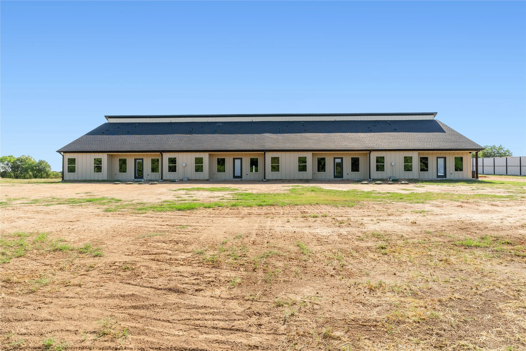 Single-story structure with light-colored siding, multiple windows, and a dark shingled roof