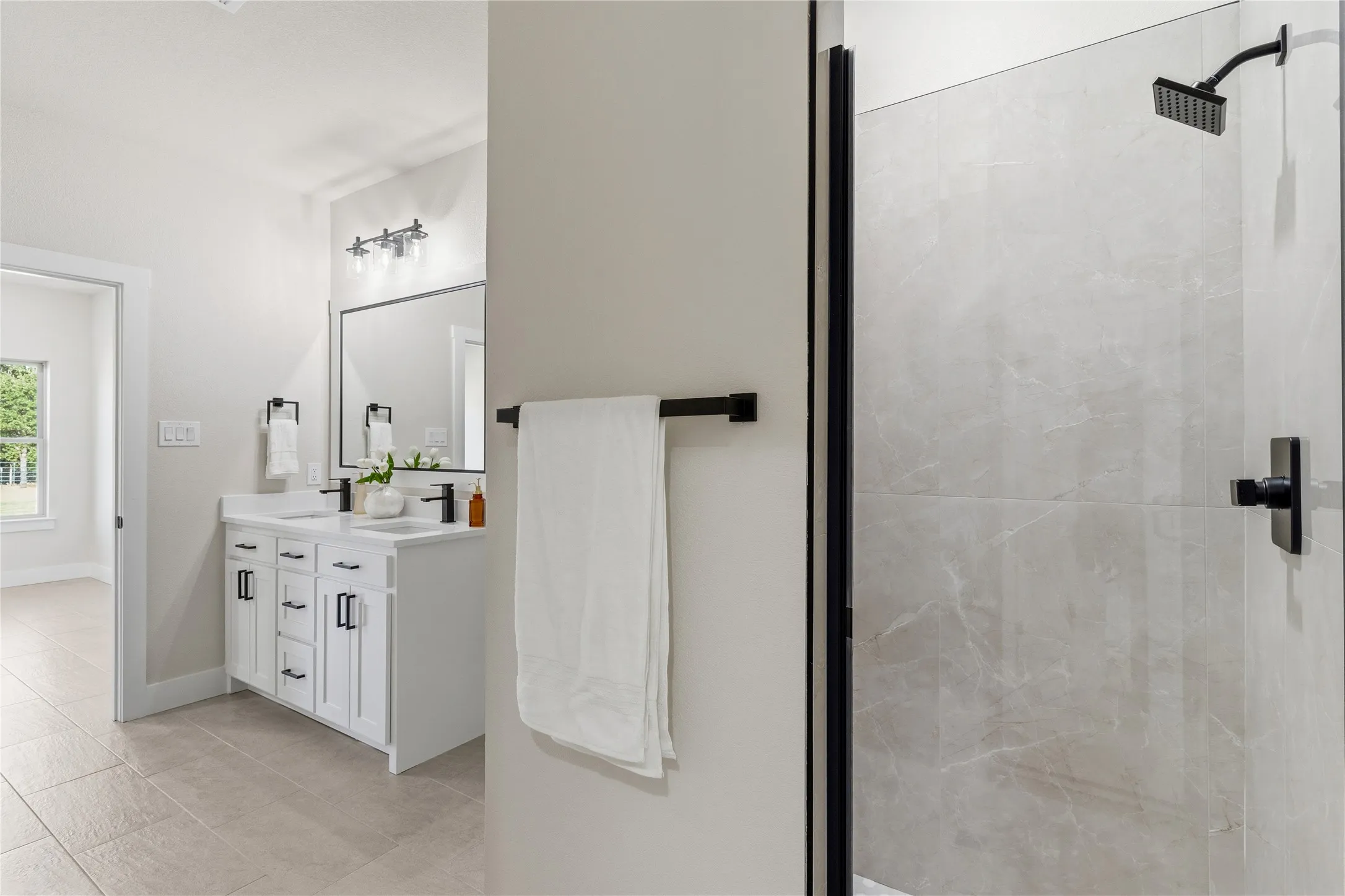 Double vanity with white cabinetry, matte black hardware, and an expansive shower with light-toned wall tile