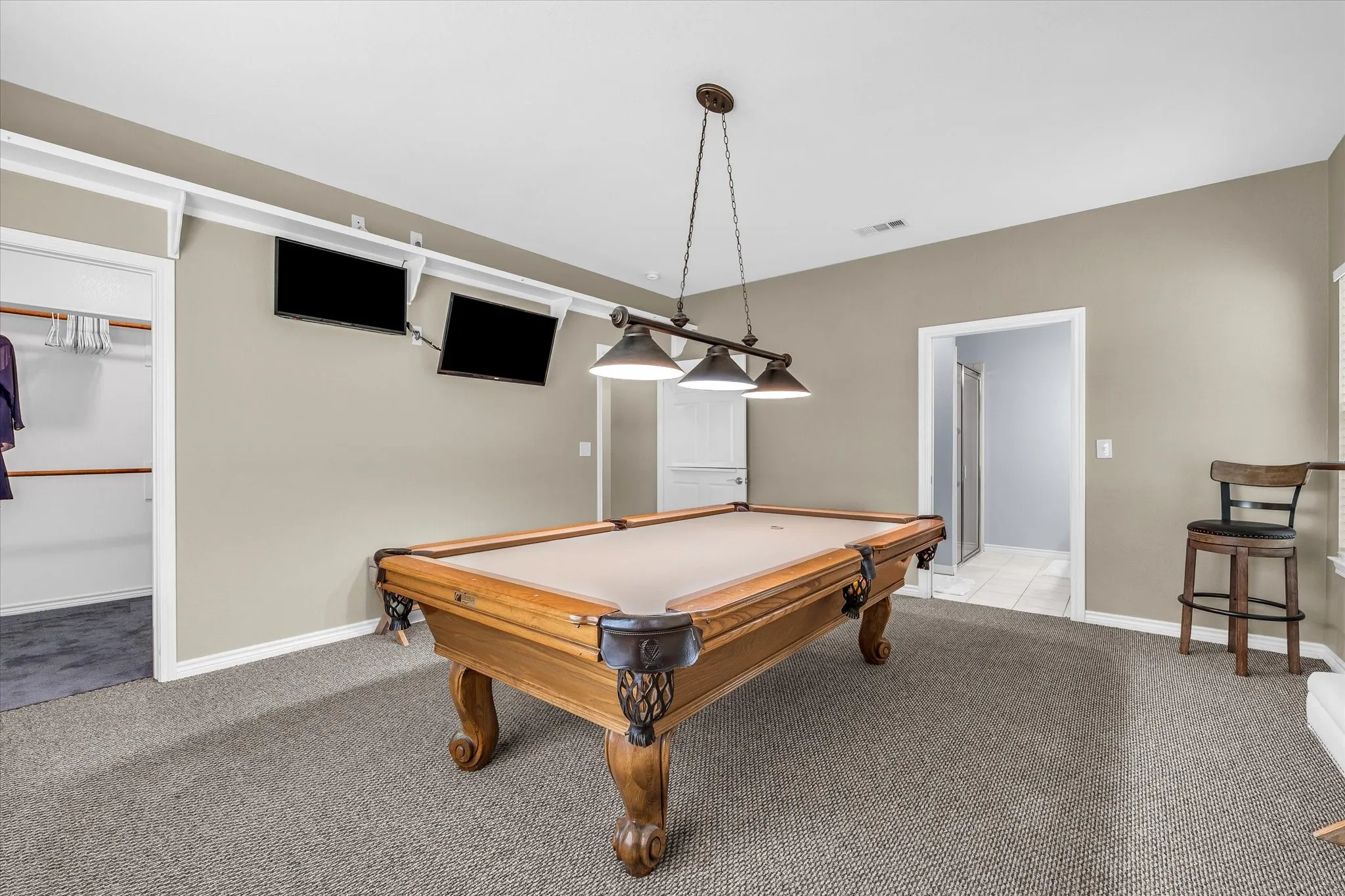 Recreation area featuring a pool table with a multi-bulb pendant light fixture, wall-mounted display screens, and a built-in closet with shelving