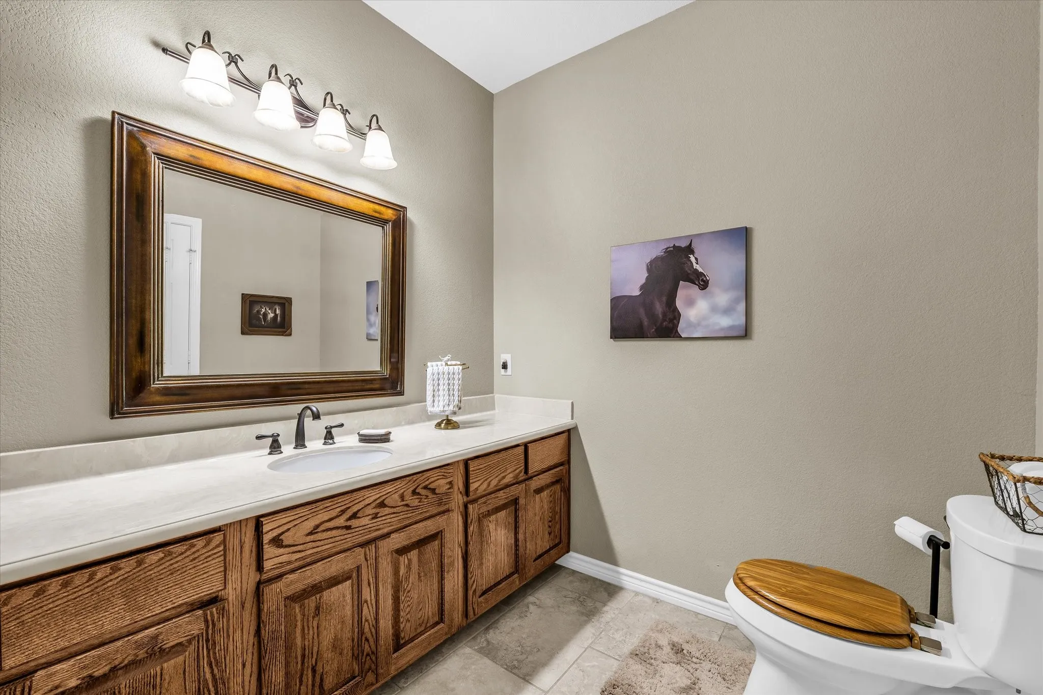 Bathroom featuring a wood-finish vanity with ample storage, a white countertop, an undermount sink, and a framed mirror