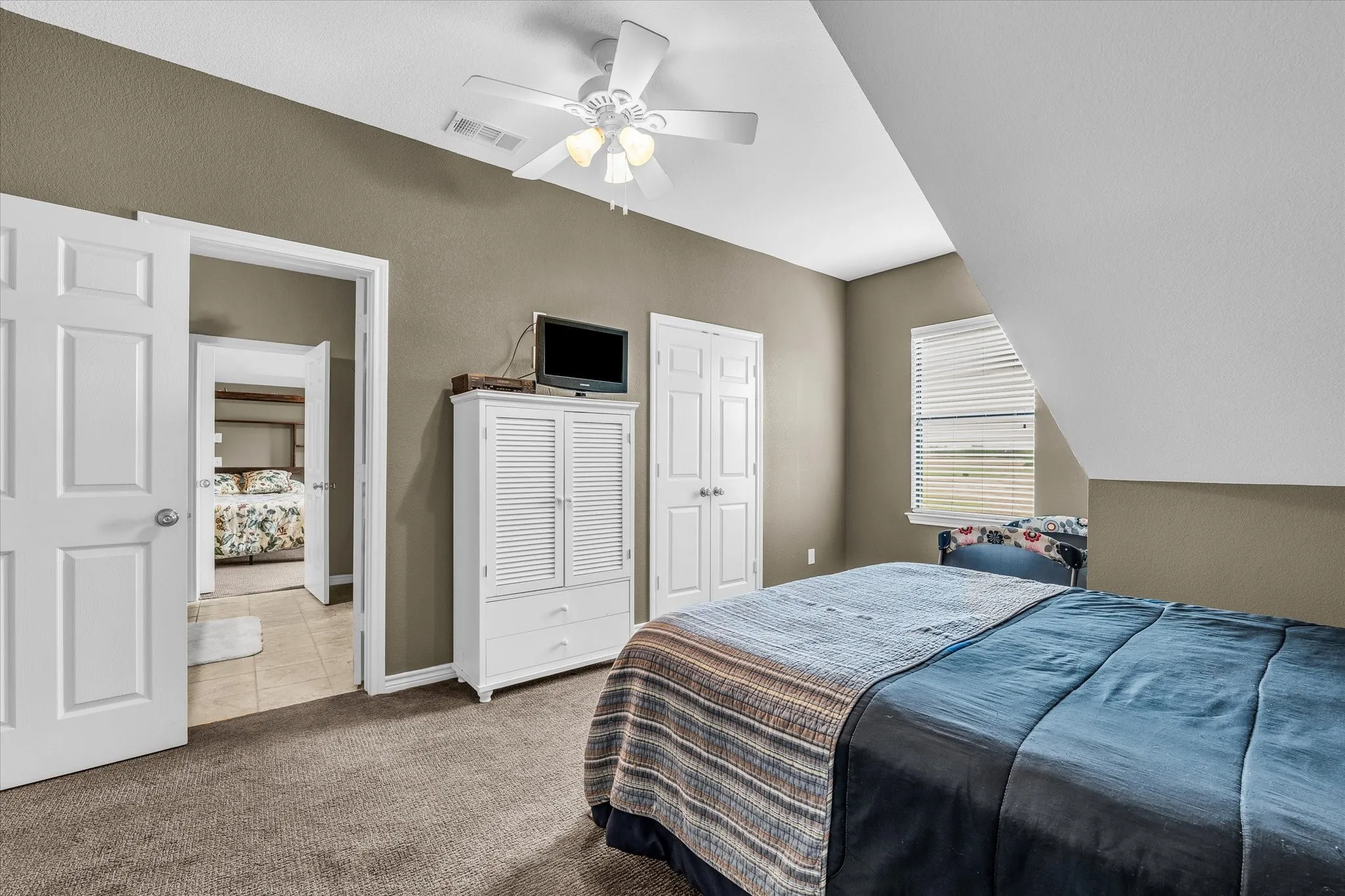 Carpeted room featuring a ceiling fan with light fixture, a window with horizontal blinds, and a sloped ceiling detail