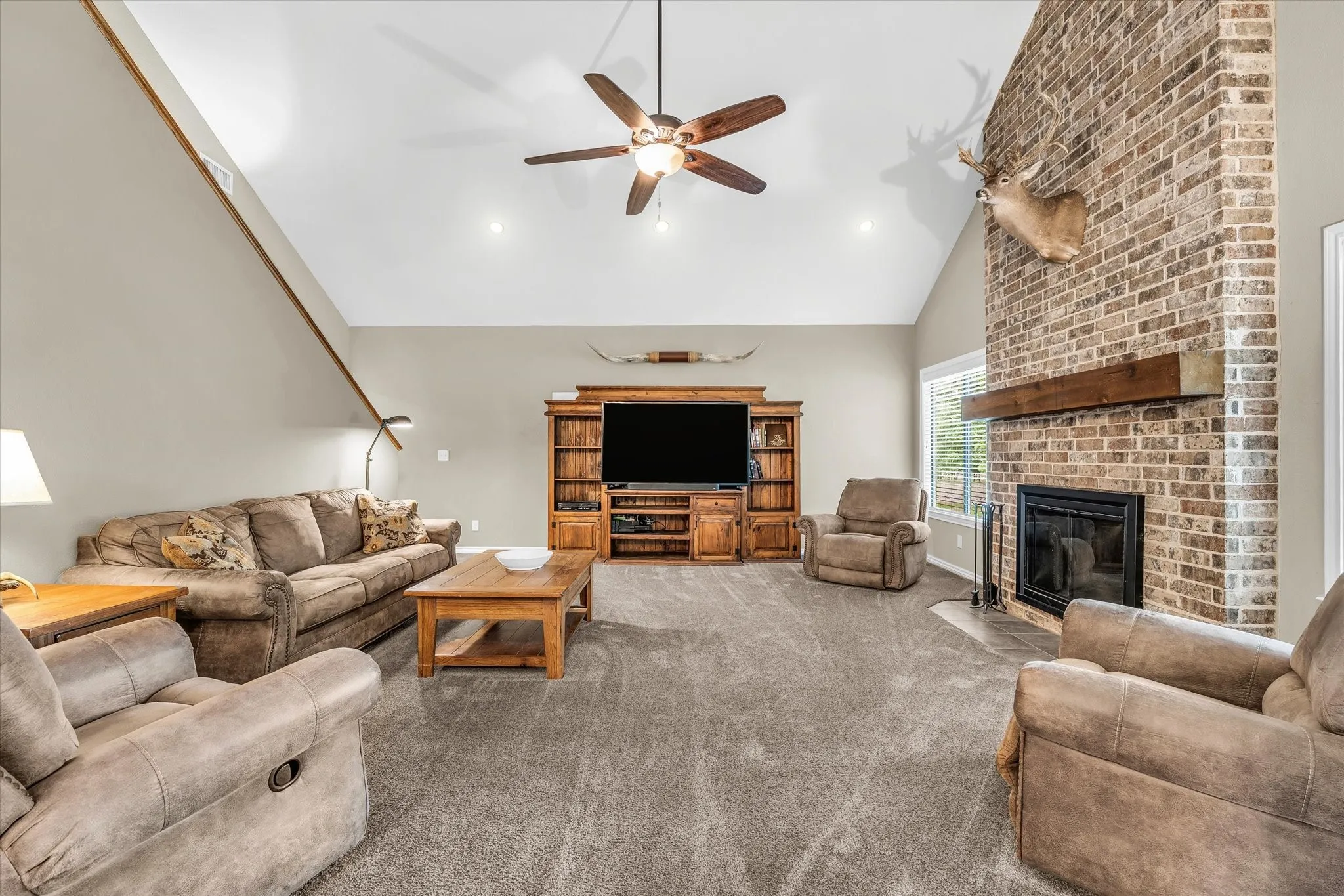 Living room featuring a vaulted ceiling with recessed lighting, a ceiling fan, and a floor-to-ceiling brick fireplace with a wood mantle