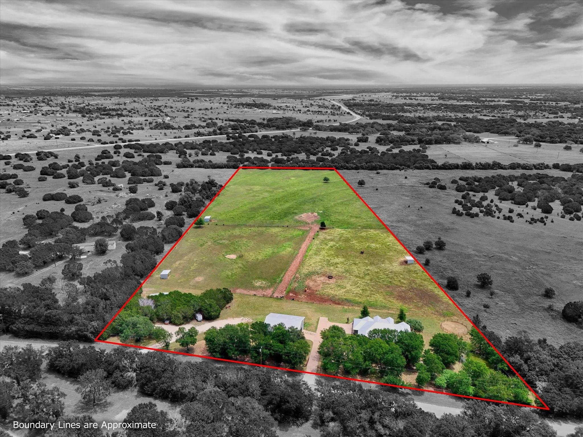 Expansive rural property featuring two residential structures, a large open field, varied tree coverage, and a defined boundary line