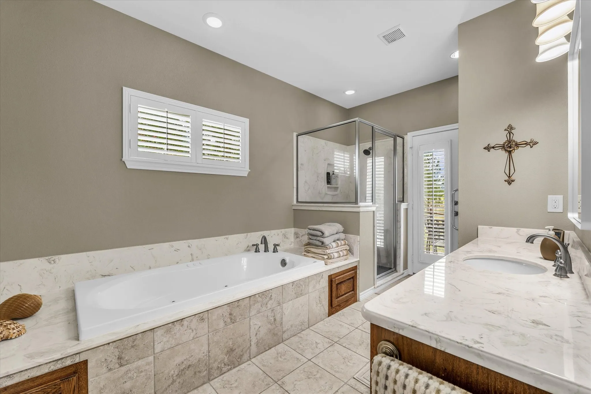 Bathroom featuring a built-in soaking tub, a glass-enclosed shower, a double vanity with undermount sinks, and a large window with plantation shutters