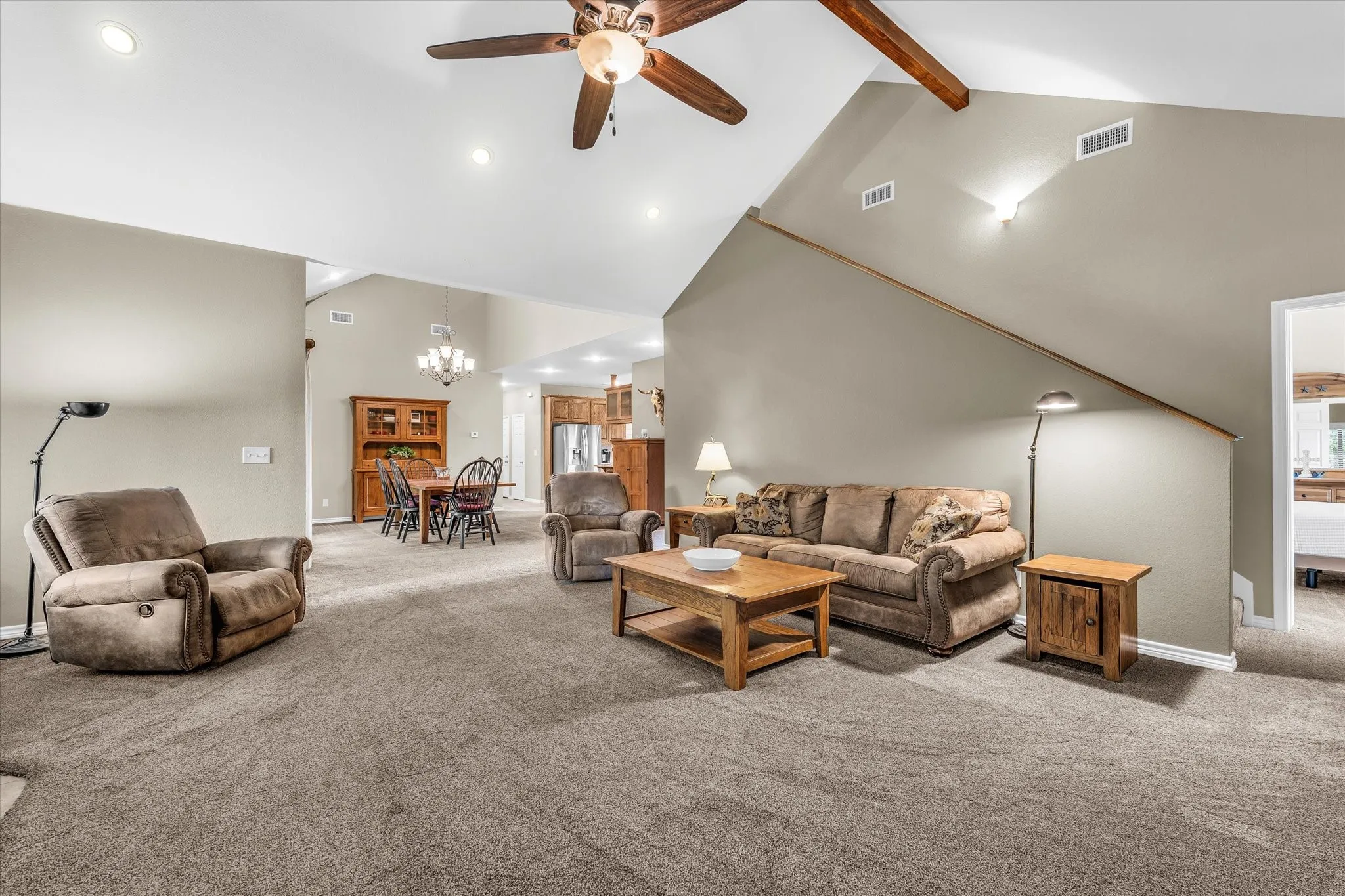 Spacious living area featuring vaulted ceilings with exposed wood beams and a ceiling fan