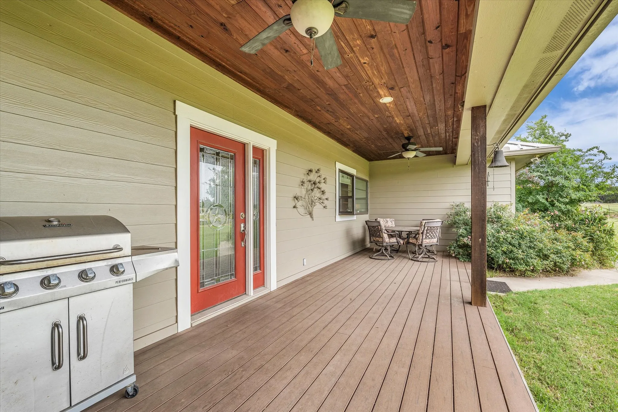 Spacious outdoor patio featuring composite decking, a wood-paneled ceiling with two ceiling fans, and light-toned siding