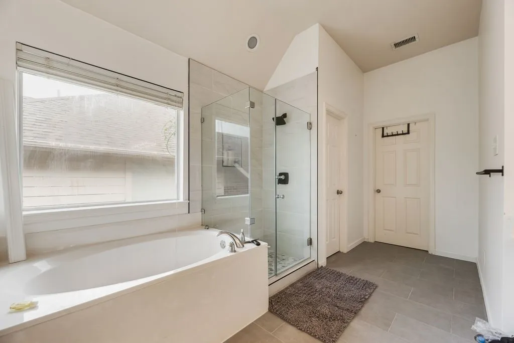 Modern bathroom featuring a built-in soaking tub with a surrounding light-toned countertop, a glass-enclosed shower with dark fixtures, and large format grey floor tiles