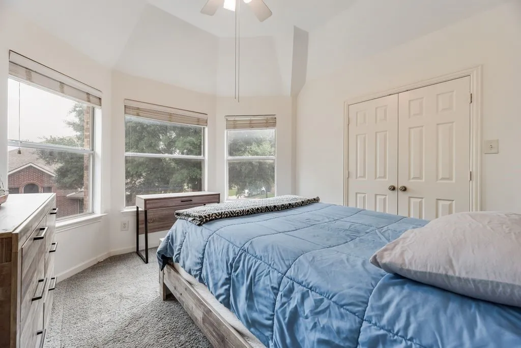 Vaulted ceiling with a ceiling fan, three pane windows with horizontal blinds, carpeted flooring, and white bifold closet doors