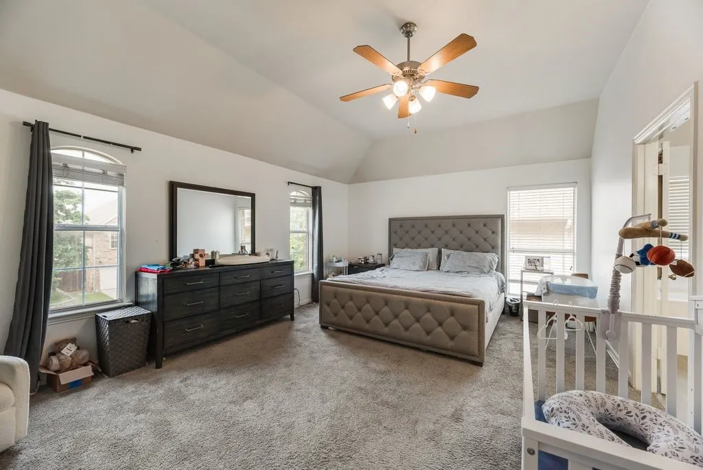 Spacious bedroom featuring vaulted ceilings, a ceiling fan with light fixture, and plush carpeting