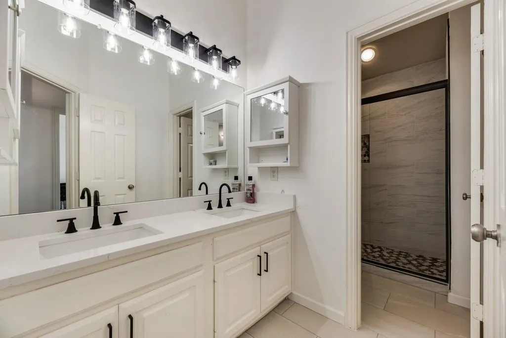 Double vanity with white cabinetry and matte black fixtures, featuring a large mirror and overhead lighting