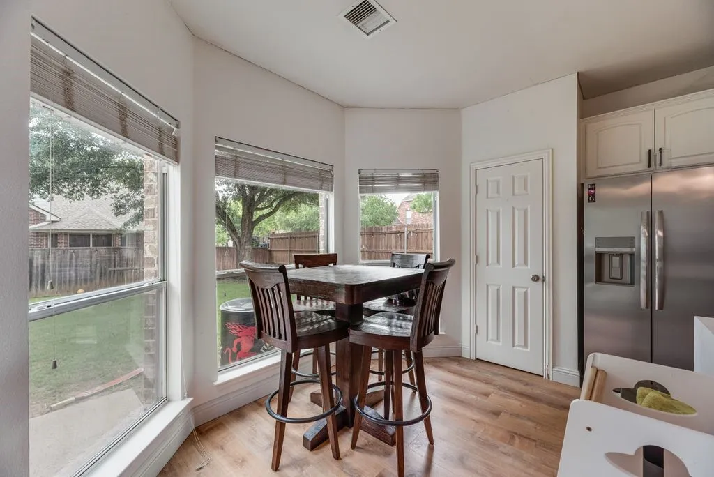 Bright dining nook featuring multiple windows, wood-finish flooring, white paneled door, and kitchen cabinetry with a stainless steel refrigerator
