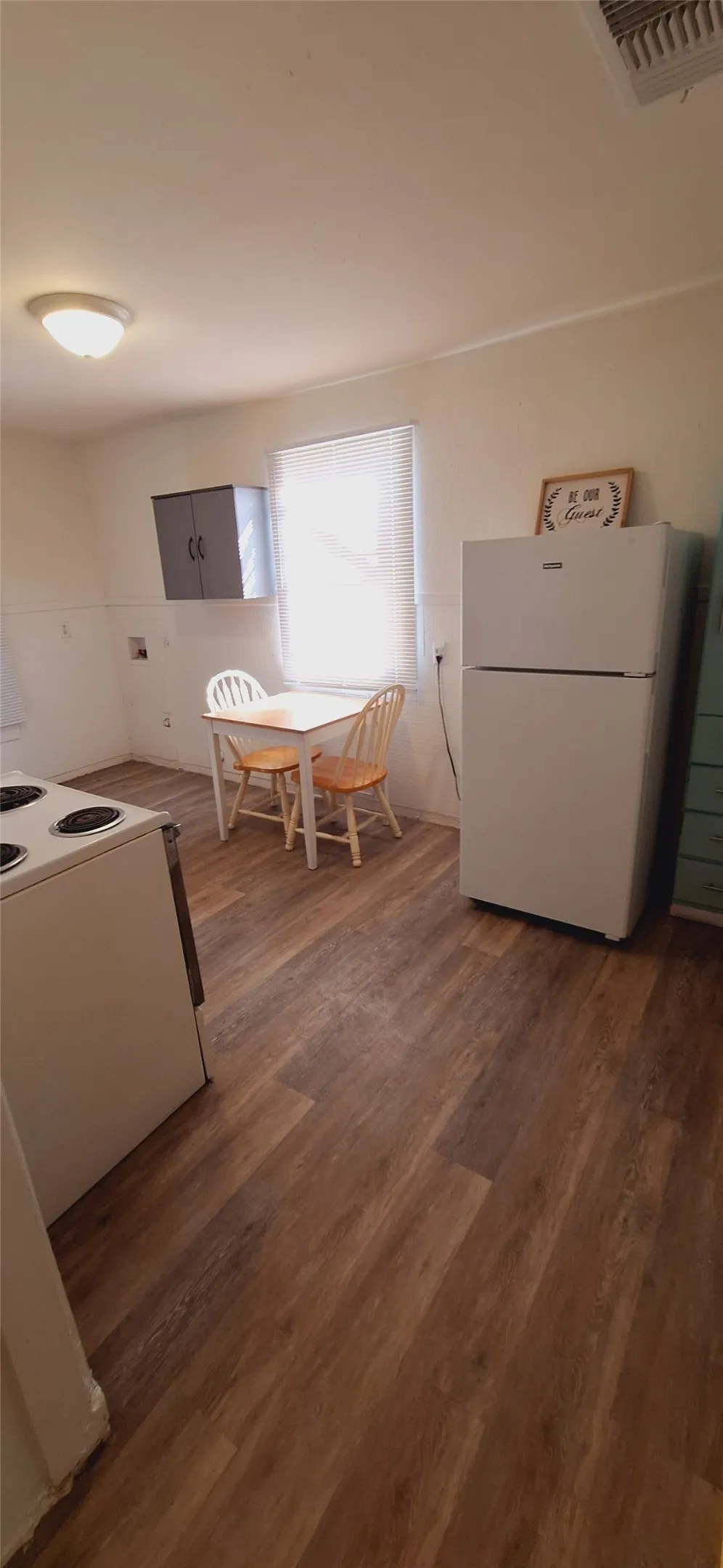 Kitchen with wood-finish flooring, a window with blinds, and a built-in upper cabinet