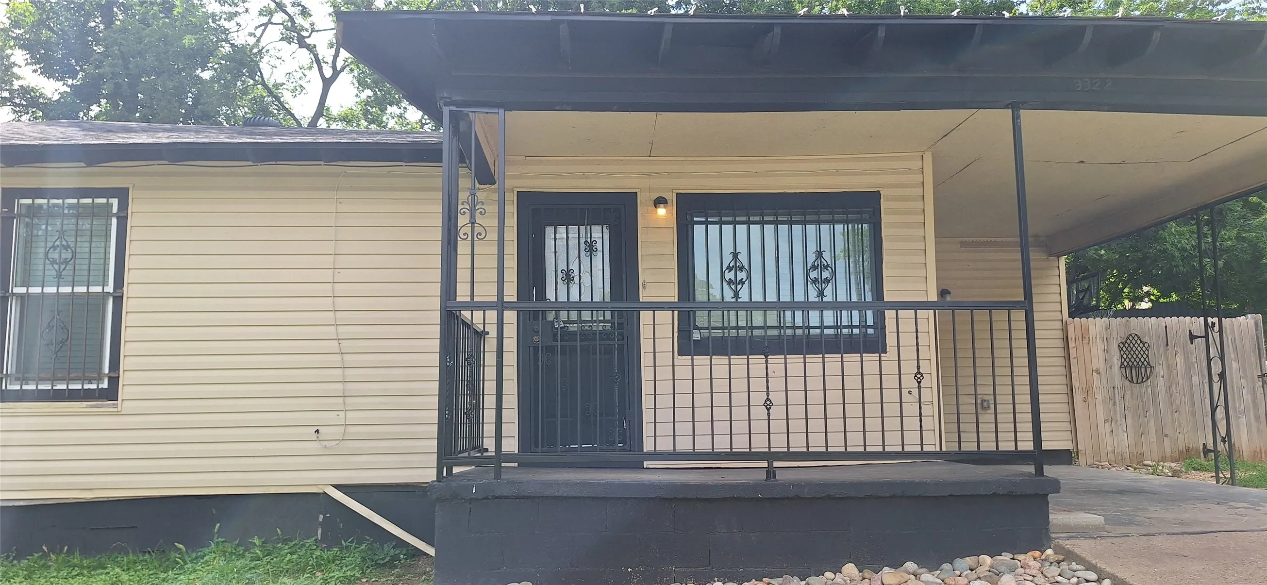 Single-story residence featuring light-toned horizontal siding, a covered front porch with black iron railings, and a black security door