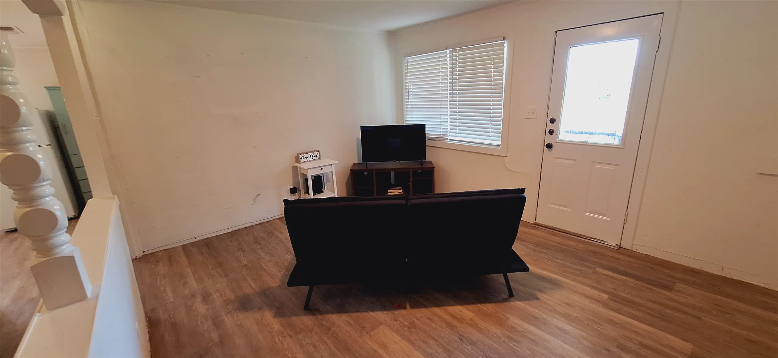 Living area featuring wood-finish flooring, white painted walls, and a window with horizontal blinds