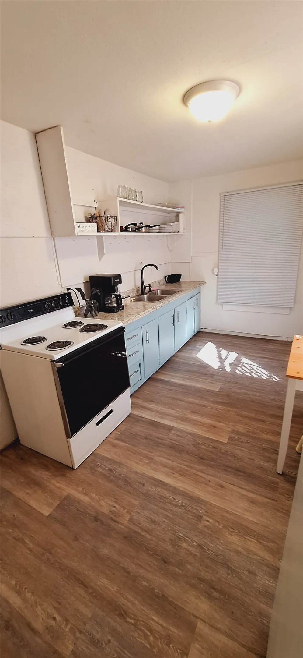 Kitchen featuring wood-finish flooring, a freestanding range, light blue lower cabinetry, open shelving, and a single basin sink with a matte black faucet