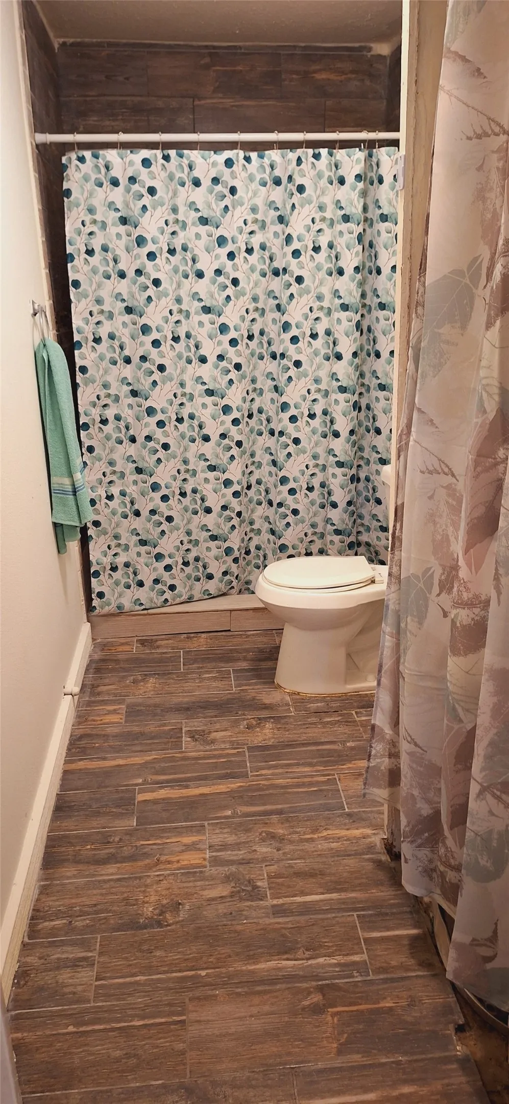 Bathroom featuring plank-style wood-finish flooring, a white toilet, and a shower area with wall tile
