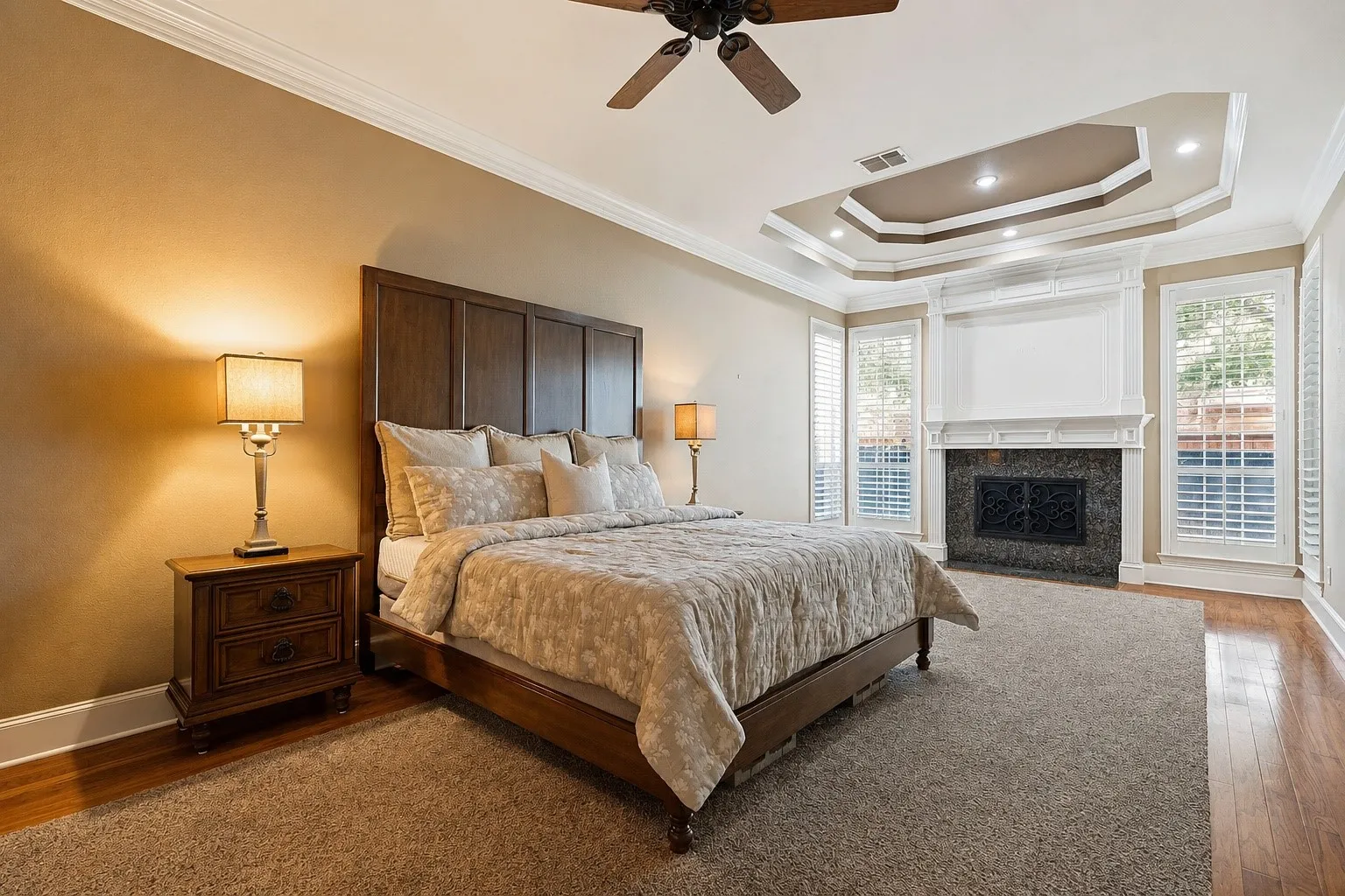 Room featuring a tiered tray ceiling with fireplace, recessed lighting, crown molding, and a ceiling fan