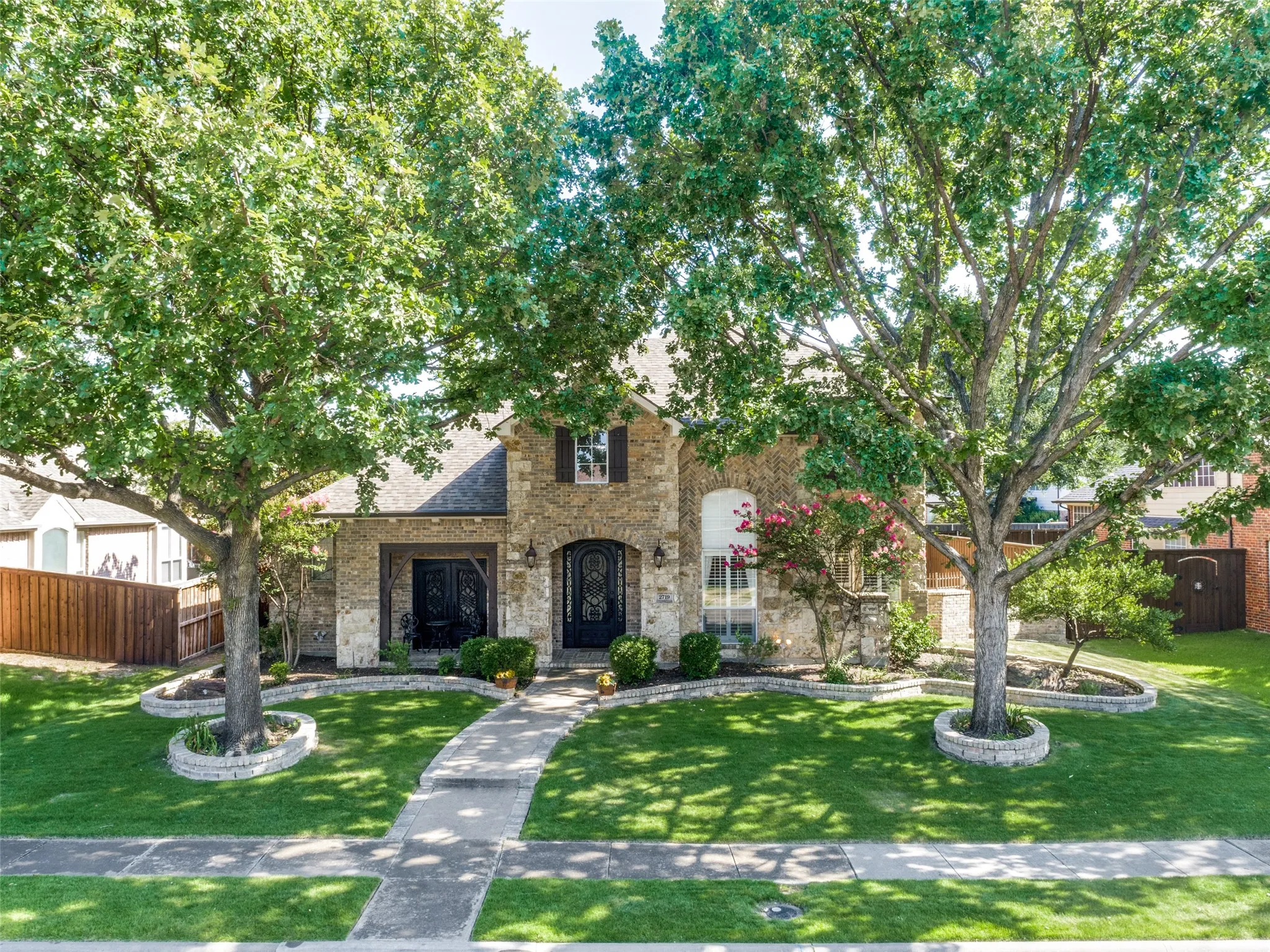 Stone facade residence featuring a covered entry, arched doorways, and symmetrical front landscaping