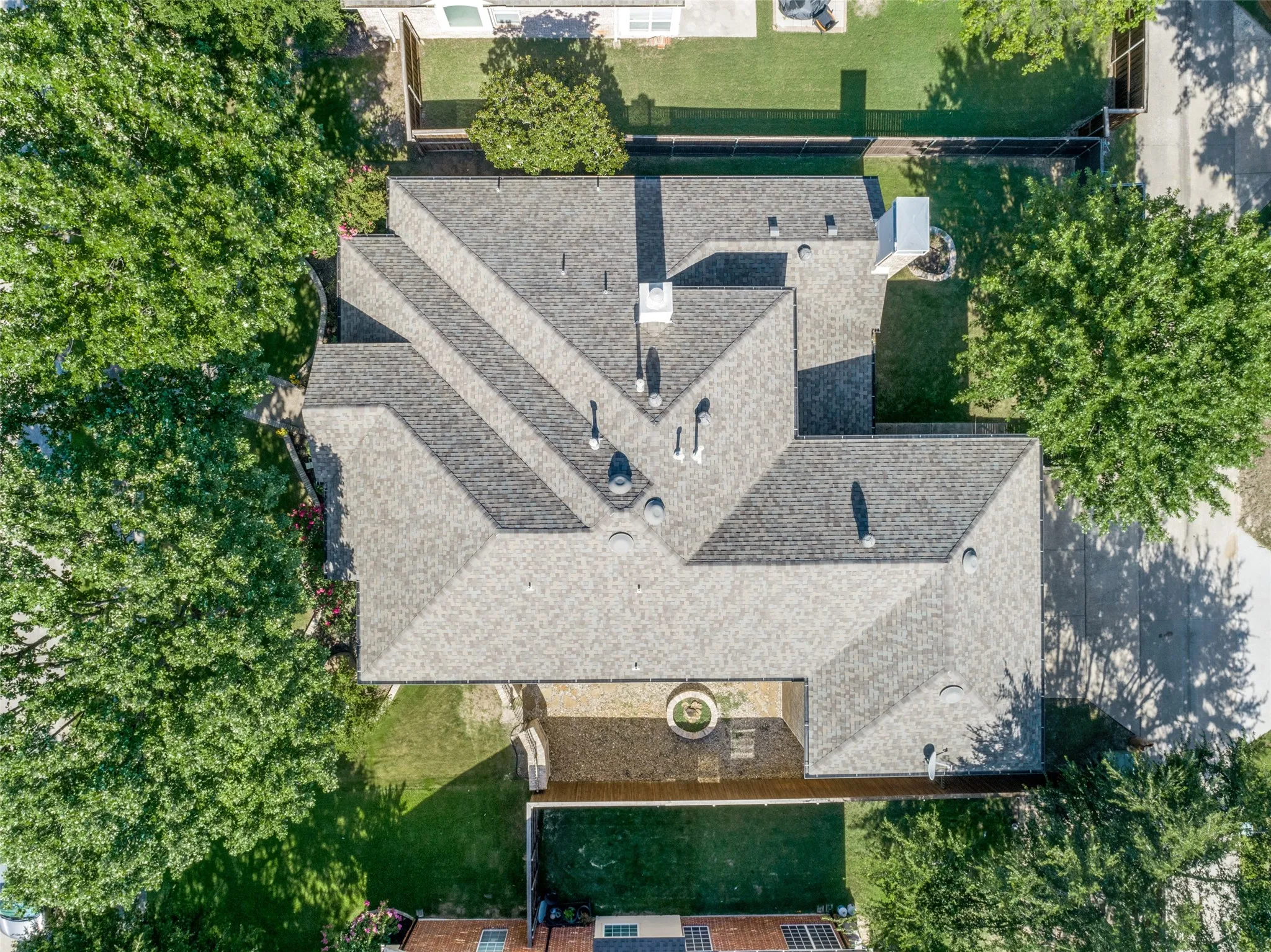 Aerial view showcasing the property's composite shingle roof, established landscaping with mature trees, and a private enclosed courtyard