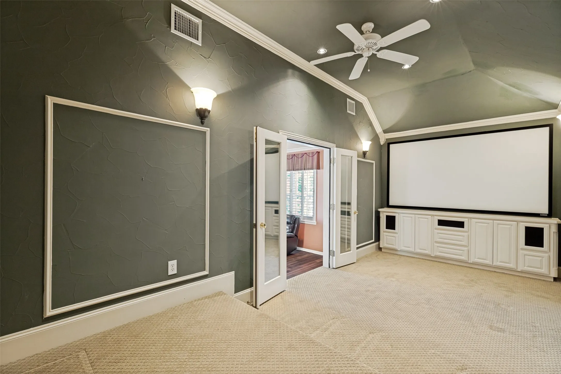 Spacious room featuring a large projector screen, built-in media cabinetry, and textured walls with sconce lighting
