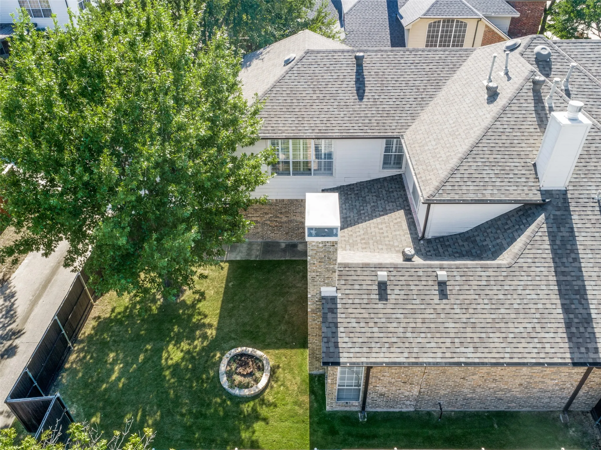 Expansive backyard featuring a manicured lawn, mature tree, and a built-in fire pit