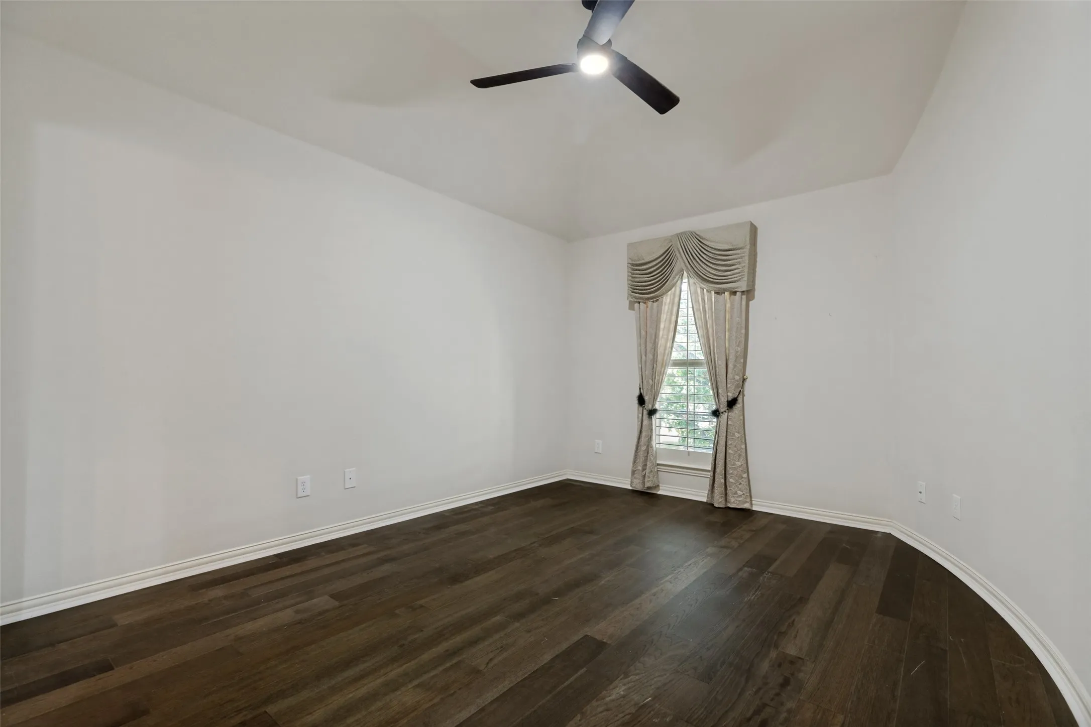 Room featuring dark wood-finish flooring, white baseboards, and a vaulted ceiling
