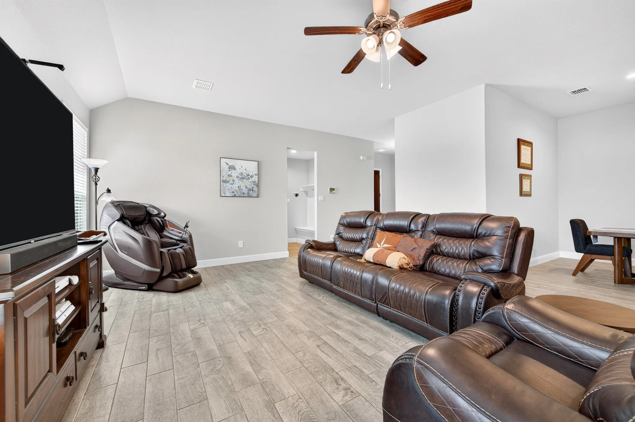 Spacious living area featuring wood-finish flooring, vaulted ceilings, and a ceiling fan with integrated lighting
