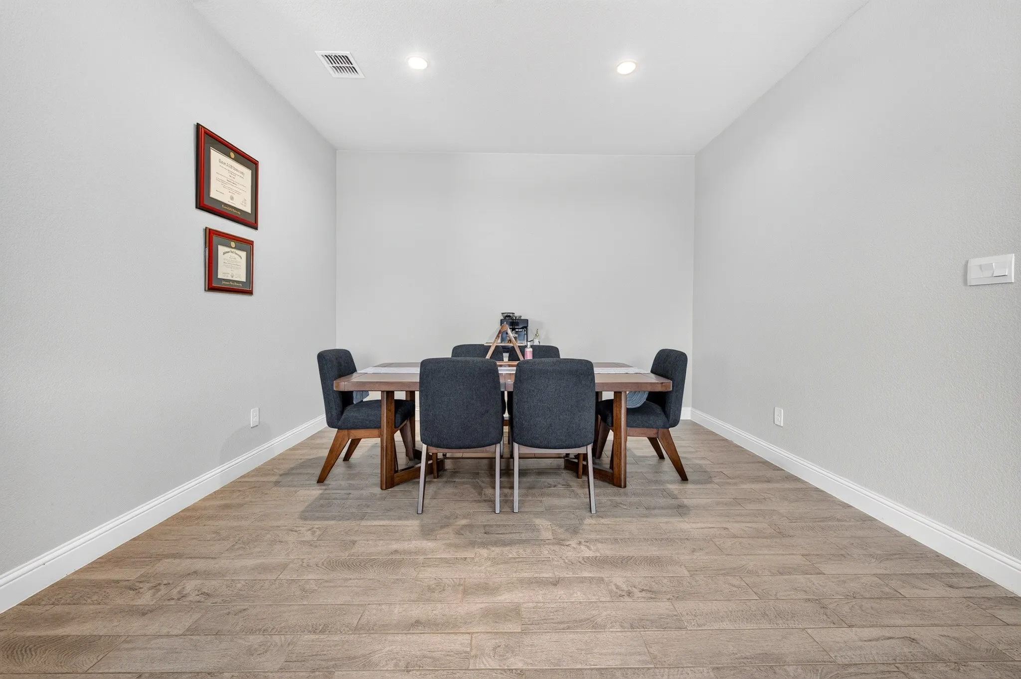 Recessed lighting illuminates the dining area, featuring wood-finish flooring and white baseboards