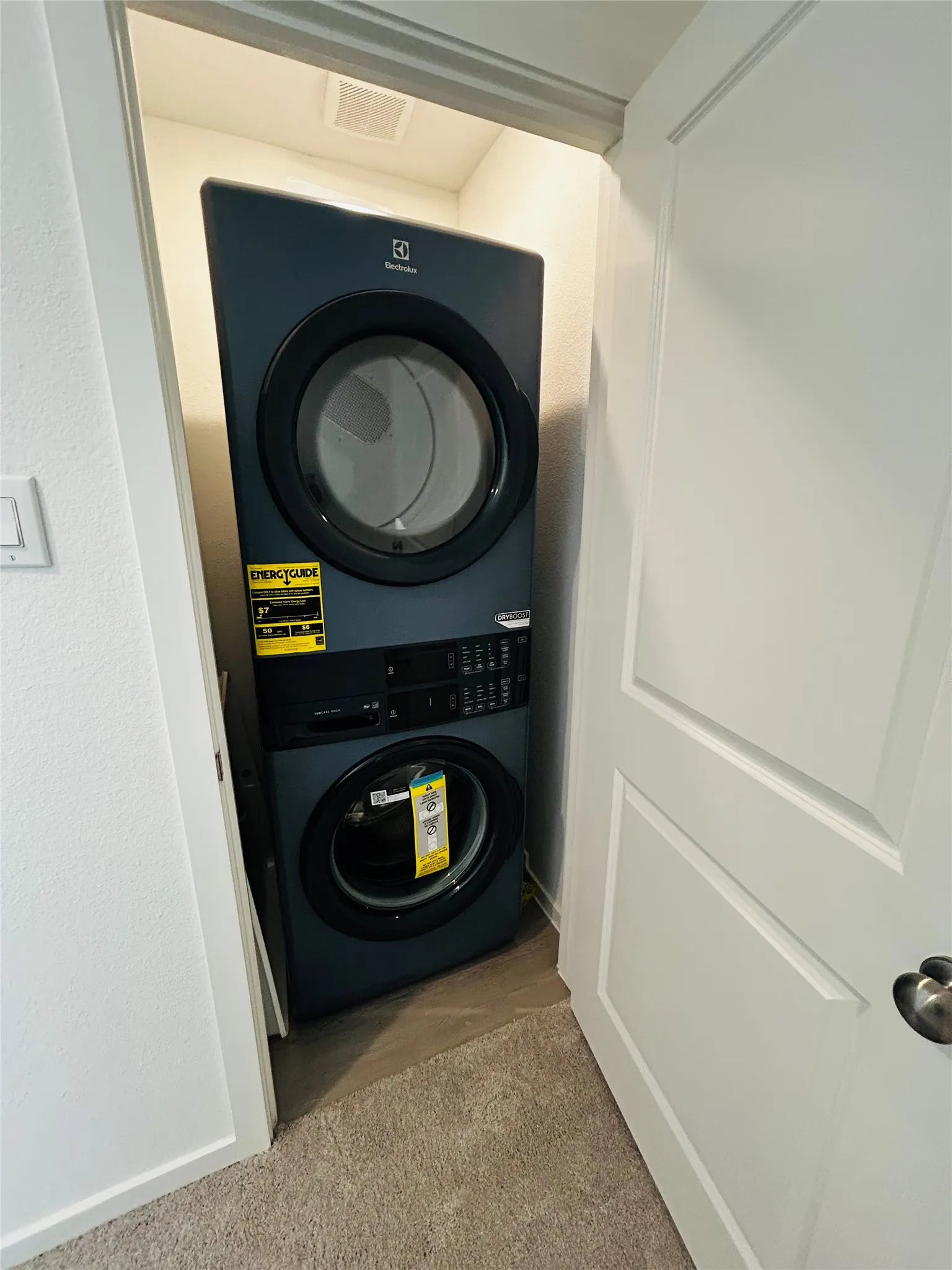 Stackable washer and dryer unit in a dedicated alcove with a paneled door