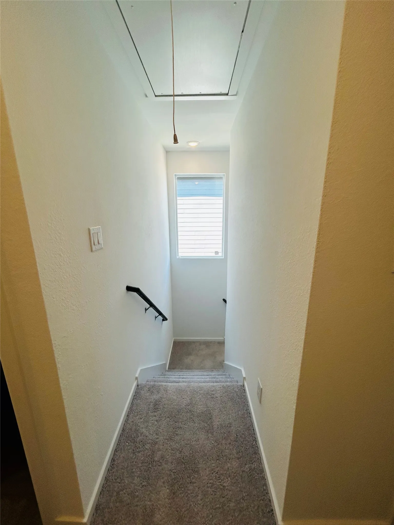 Carpeted staircase with a black handrail, recessed lighting, and a window with blinds