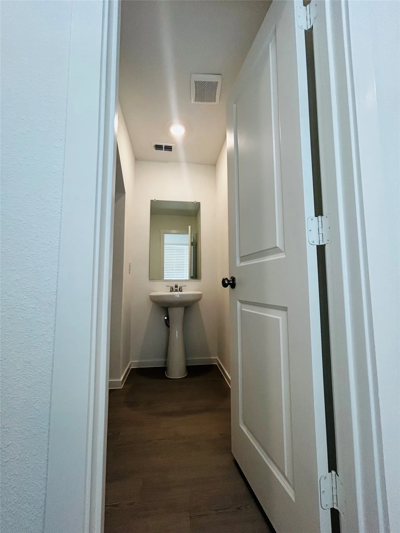 Dedicated half bath featuring a pedestal sink, recessed lighting, and wood-finish flooring throughout a bright, linear hallway with white painted walls and panel doors