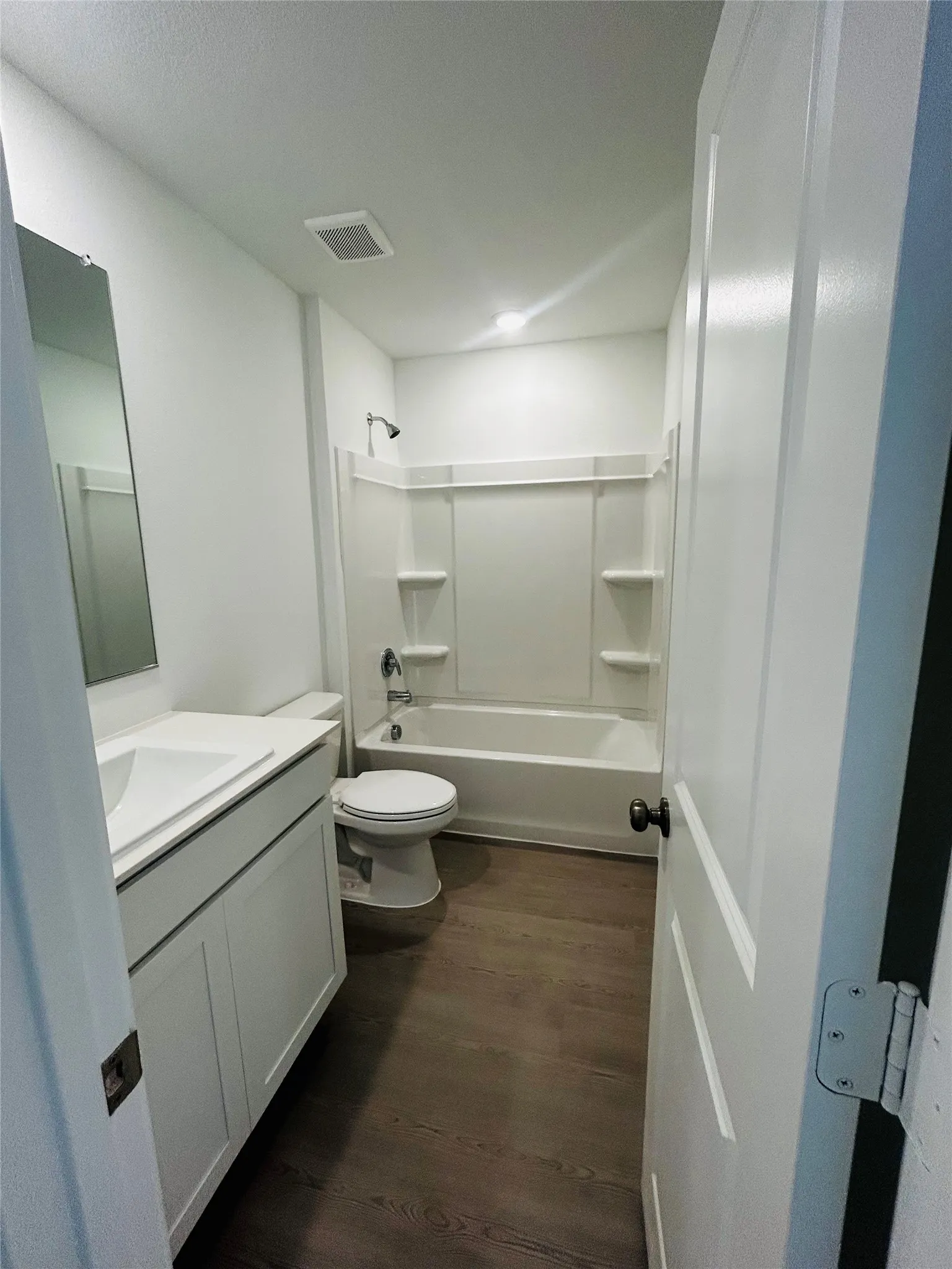 Full bathroom with a white vanity, integrated sink, overhead lighting, and wood-finish flooring