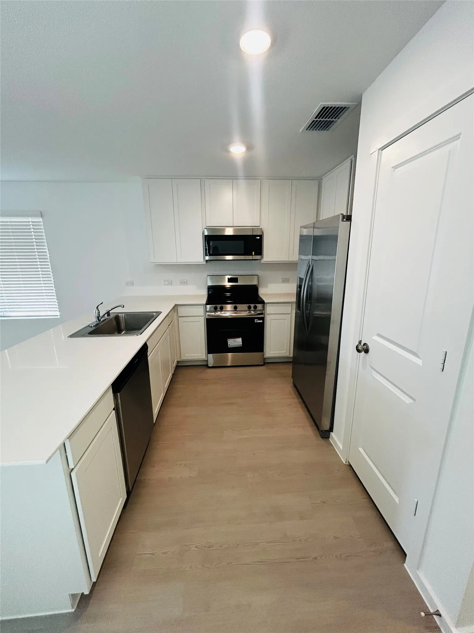 Modern kitchen featuring white cabinetry, light-toned wood-finish flooring, stainless steel appliances, recessed lighting, and light countertops