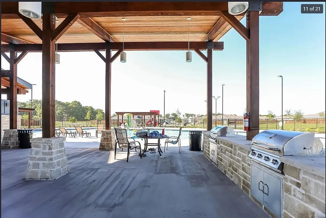 Spacious covered patio featuring a full outdoor kitchen with built-in stainless steel grills and extensive stone-finish bar seating