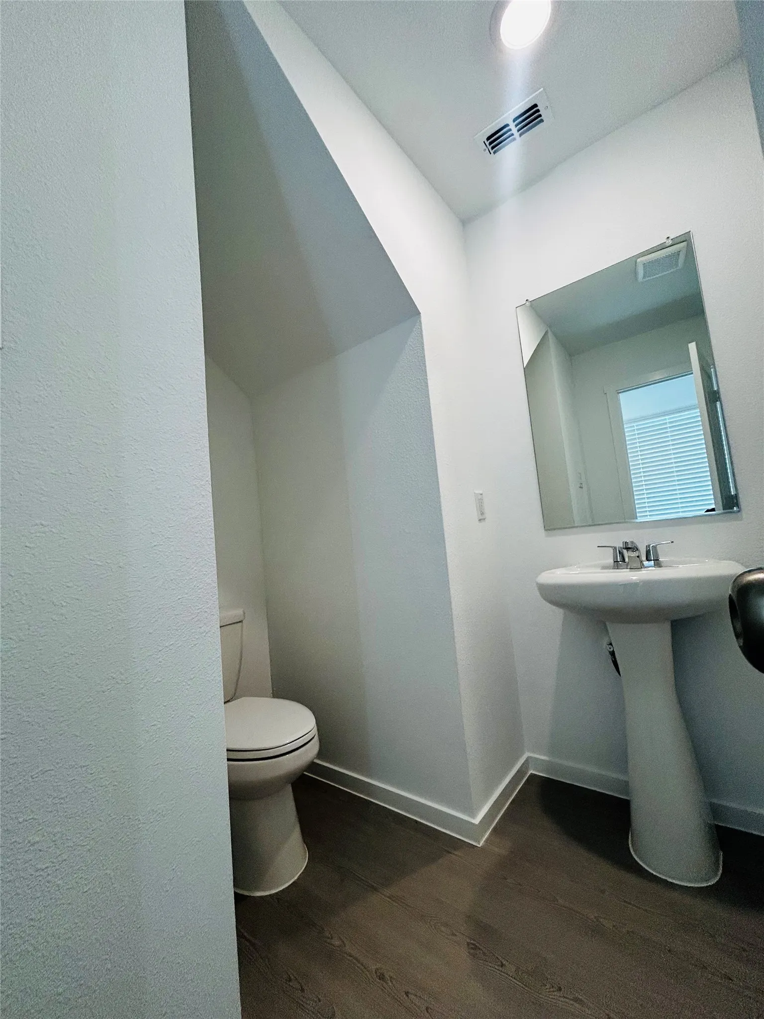 Pedestal sink with chrome fixtures, wall-mounted mirror, wood-finish flooring, and recessed ceiling lighting