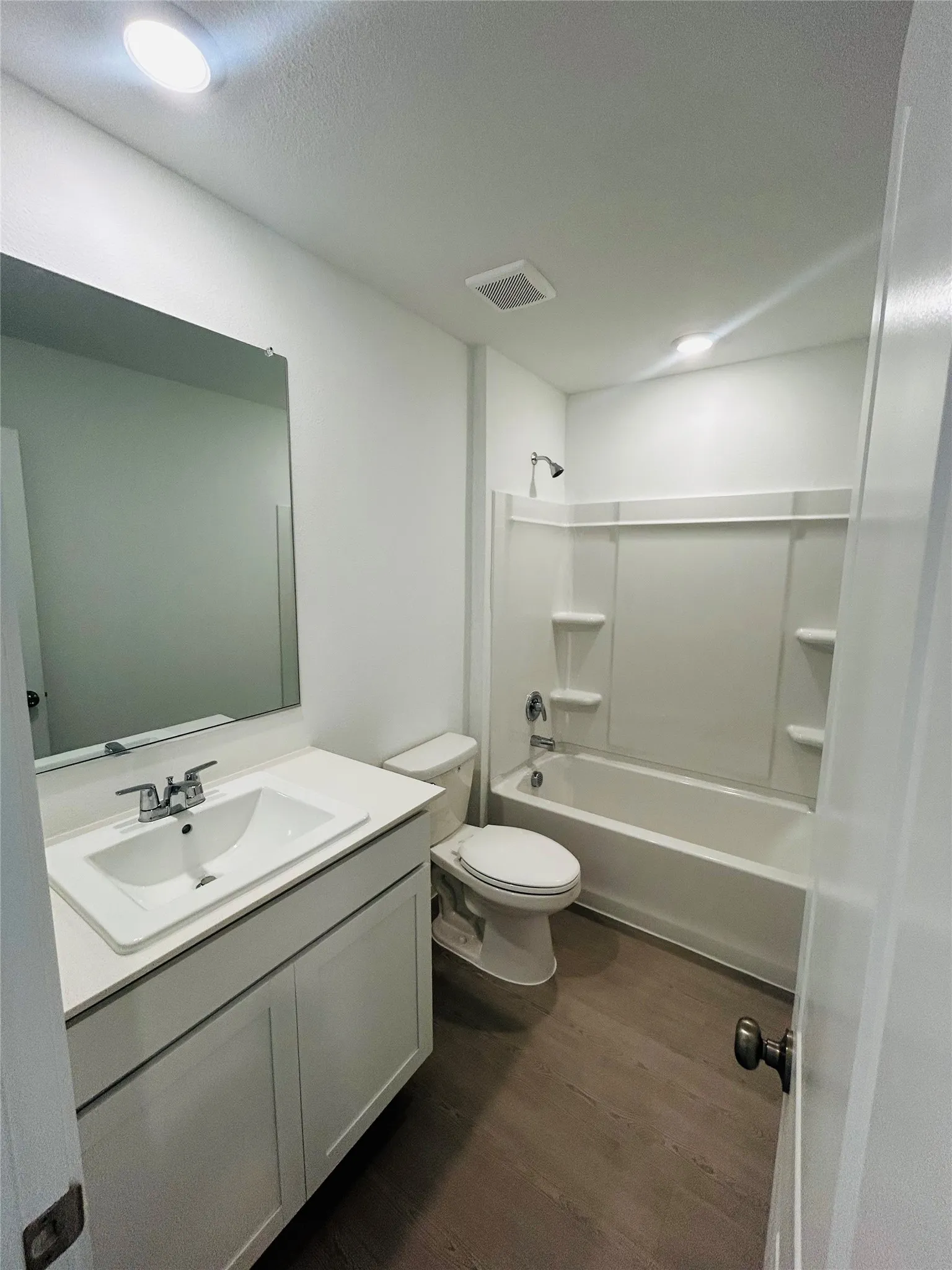 Bathroom featuring a single vanity with an integrated sink, polished chrome faucet, white cabinetry, and wood-finish flooring